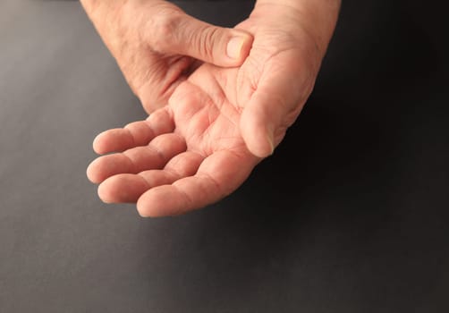 A senior man grips his sore hand on a black background with copy space.