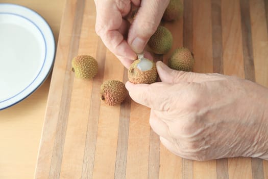 A man begins to peel a fresh lychee on a cutting board.