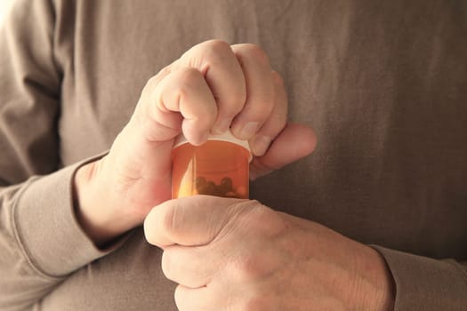 Older man struggles to get a container of capsules open.