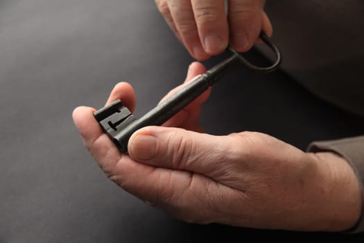 An older man holds a large, antique key on a black background.
