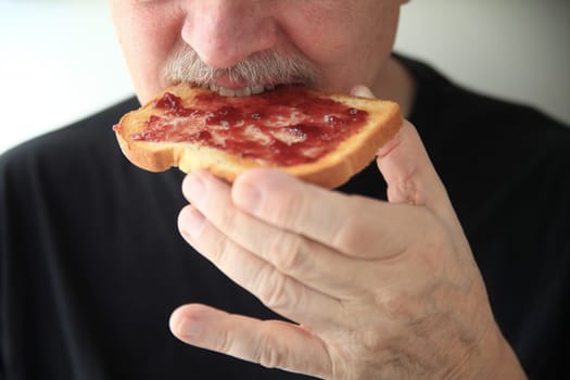 Senor man eating buttered toast spread with grape jam