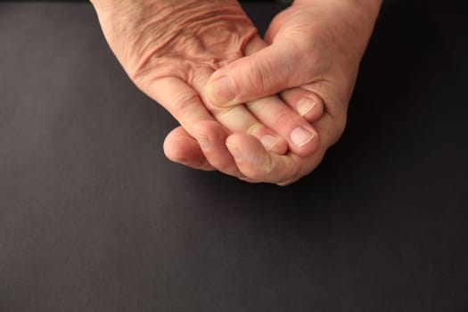 Senior man grasps the numb fingers of his other hand.