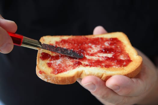 An older man has spread grape jam on his buttered toast