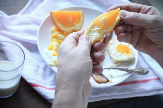 A man has fresh orange pieces with his eggs and bacon breakfast.