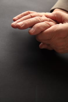 A man grips his aching hand on a dark background with copy space.