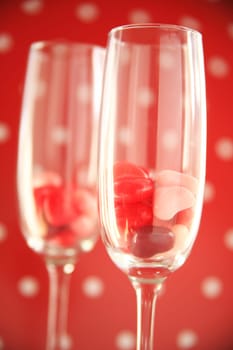 Two wine flutes with candy hearts against a red and white polka dot background