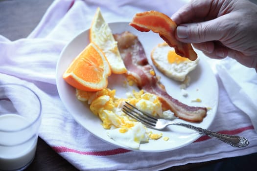 Point-of-view shot of a scrambled eggs, bacon and fresh orange breakfast by a window with morning light