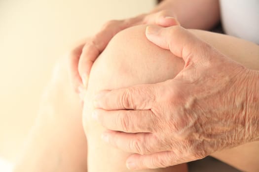 A senior man holds his aching knee in both hands.