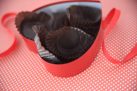 Heart-shaped candy box with empty wrappers inside on polka dot background with red ribbon
