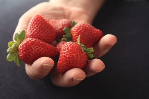 A man holds fresh, ripe strawberries in his hand on a black background.