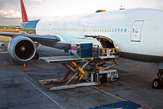 Loading cargo or luggage into airplane at airport on a cloudy day.