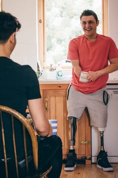 quadriplegic man standing in his kitchen. He is having a conversation with his friend and they are both drinking tea.