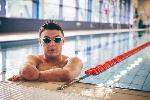 Quadriplegic swimmer posing for the camera at the side of the pool. He is wearing goggles.