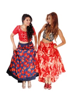 Two lovely woman in colorful outfits standing and lifting up there.skirts, showing there heels, isolated for white background..