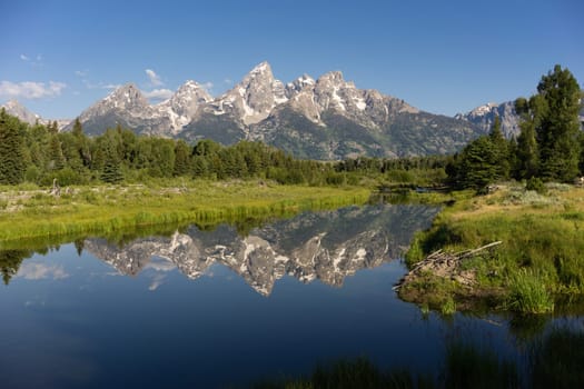The water is perfectly smooth showing high peak reflections in the Teton's