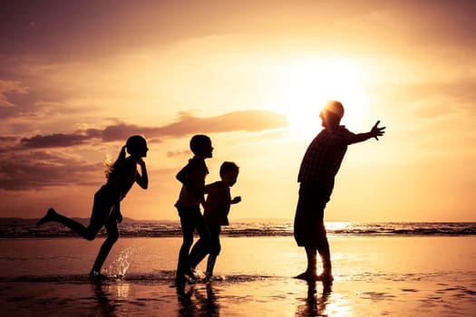 Father and children playing on the beach at the sunset time. Concept of friendly family.