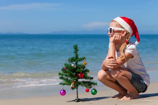 Happy little girl sitting on the beach at the day time. Concept of Happy New Year.
