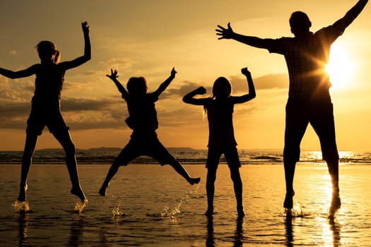 Father and children playing on the beach at the sunset time. Concept of friendly family.