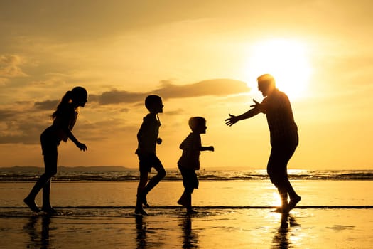Father and children playing on the beach at the sunset time. Concept of friendly family.