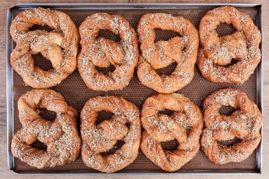 Soft pretzels spread with nuts and sugar holding on brown waxed paper in a stainless steel tray