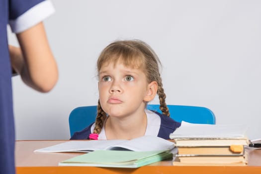 Schoolgirl sitting at the desk angrily looks at another girl