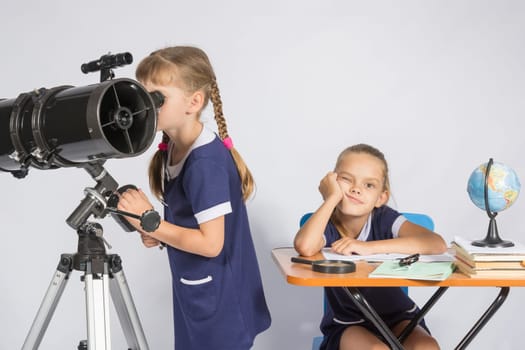 A girl looks through a telescope, the other girl is waiting sad results