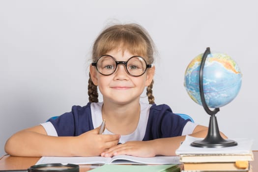 Happy girl first grader sits at a table
