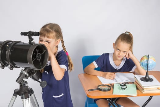 Girl astronomer looks at the sky through a telescope, the other girl is sitting at the table