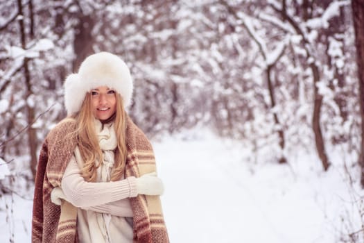 beautiful blonde girl is standing in a blanket in the woods, smiles, big hat on his head and mittens