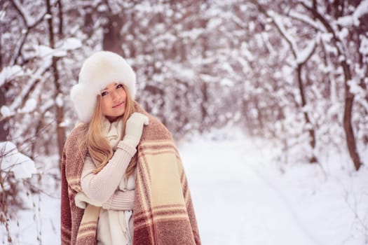 beautiful blonde girl is standing in a blanket in the woods, smiles, big hat on his head