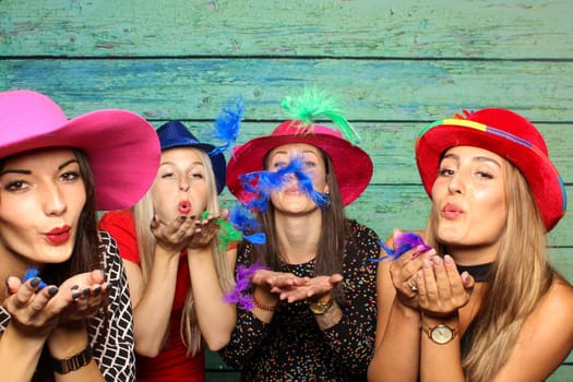 Women with hats blow colorful feathers out of their hands