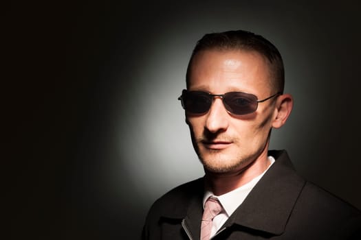 Head-and-shoulder portrait of a middle-aged man with sunglasses in front of a dark studio background with spot light.