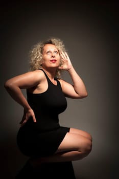 Lateral full-body view of a middle-aged woman squatting against a dark background posing.