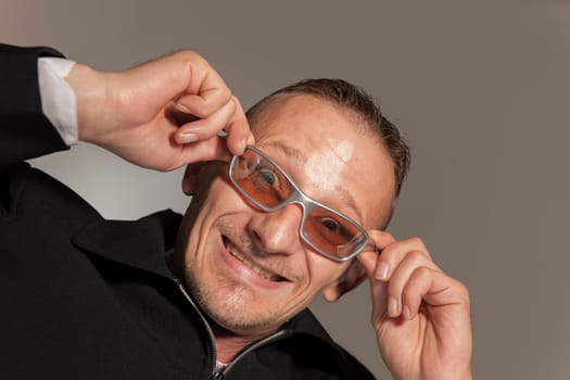 Funny head-and-shoulder portrait of a middle-aged man with sunglasses grimacing against a gray studio background.