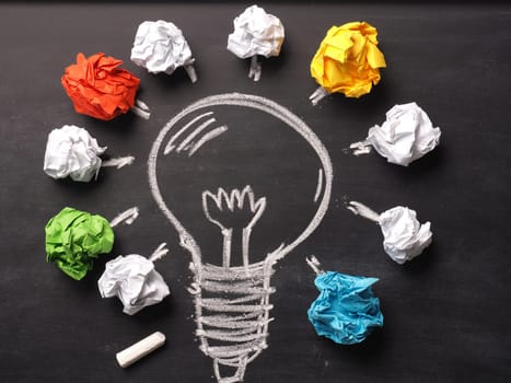 Crumpled paper on a blackboard with a handdrawn lightbulb, new idea concept background