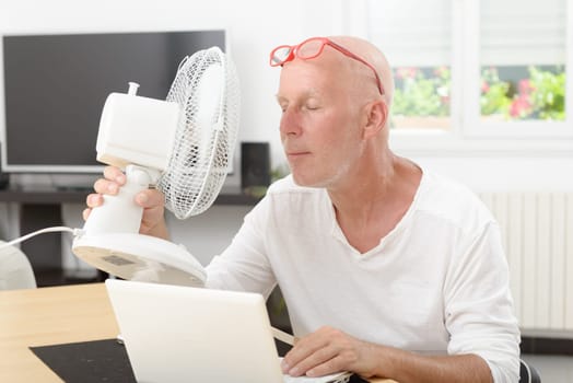 mature man refreshed with a fan in his home