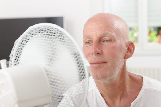 mature man refreshed with a fan in his home