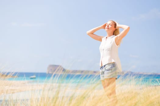 Relaxed woman enjoying sun, freedom and life an a beautiful beach. Young lady feeling free, relaxed and happy. Concept of vacations, freedom, happiness, enjoyment and well being.