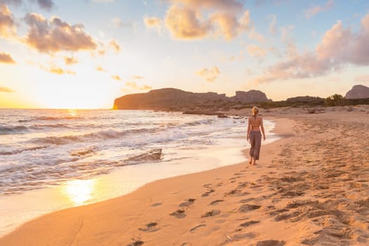 Woman walking on sand beach at golden hour. Seashore sunset walk.