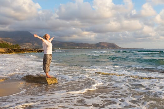 Relaxed woman, arms rised, enjoying sun, freedom and life an beautiful beach in sunset. Young lady feeling free, relaxed and happy. Concept of vacations, freedom, happiness, enjoyment and well being.