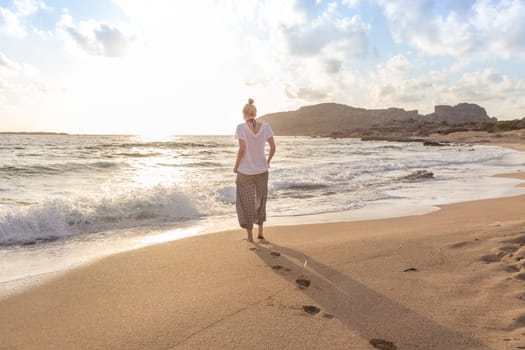Woman walking on sand beach at golden hour. Seashore sunset walk.