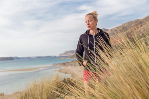 Relaxed woman in dark hoodie walking on serene Balos beach, Greece, enjoying beautiful nature and nice views.