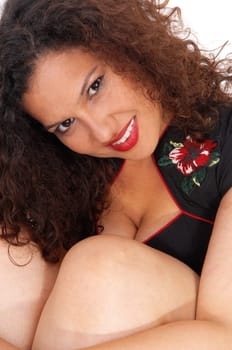 A beautiful young woman smiling and hugging her knees with curly.brunette hair, isolated for white background..