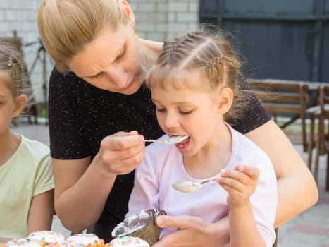Mother feeding daughter with spoon confectionery glaze for cooking cakes