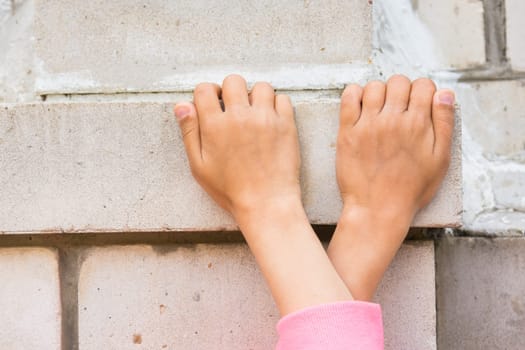 Crossed children's hands seized on the brick wall
