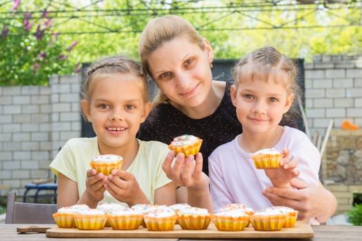 Mother and two daughters sitting at the table with Easter cupcakes in his hands and looked into the frame