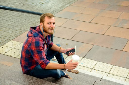 young man with soft drink sitting on stairs and using his smartphone