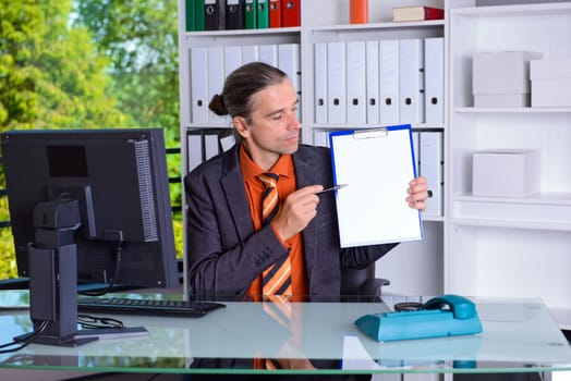 young business man in office pointing at clipboard with white page