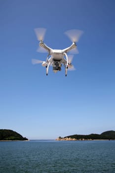 KAGAWA, JAPAN - July 6, 2016: White remote controlled Drone Dji Phantom 3 equipped with high resolution video camera hovering in air with sea and clear blue sky in the background