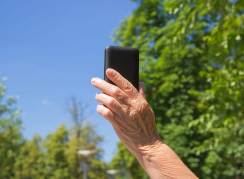 The phone in old female hand on the blue sky background